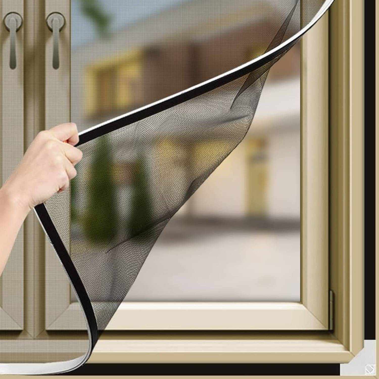 A hand lifting a black mesh magnetic window screen away from its magnetic strip